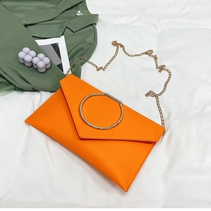 Détail macro de la pochette enveloppe orange avec poignée ronde dorée et bandoulière chaîne