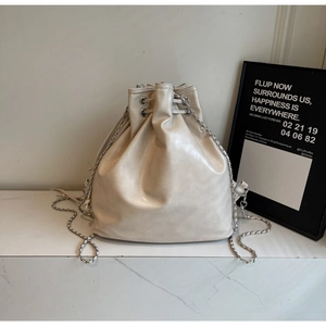 Detailed close-up of cream-colored drawstring bucket bag with metal eyelets and woven chain