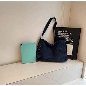 Detail of vintage navy denim hobo bag with retro metal buttons on a white stone background