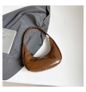 Detailansicht der braunen Hobo-Tasche mit silbernen Nieten auf grauem Anzug-Hintergrund