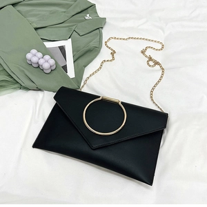Détail de la pochette enveloppe en cuir noir avec un grand anneau doré et une bandoulière