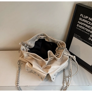 Detail view of cream drawstring bucket bag showing studded base and metal chain strap