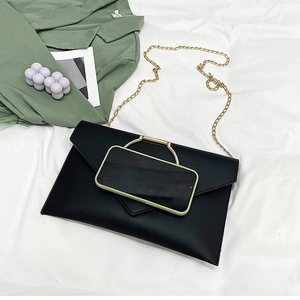 Vue détaillée de la pochette enveloppe noire avec poignée en métal et chaîne près d'un mobile