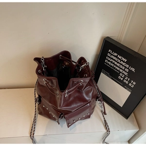 Detail of burgundy leather bucket bag featuring silver rivets and metal chain strap