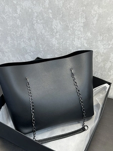 Minimalist black tote bag in matte leather with silver chain strap and gift box packaging