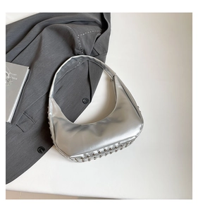Detailaufnahme der silbernen Hobo-Bag mit Punk-Metallnieten auf elfenbeinfarbenem Grund