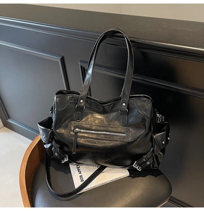 Detail of black glossy tote bag with zippers and buckle side pockets on a chair
