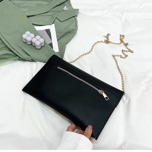 Détail de la pochette en similicuir noir avec bandoulière chaîne et poche zippée avant