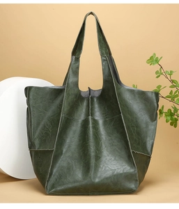 Detailed view of dark green large tote bag with soft leather texture on a beige pedestal