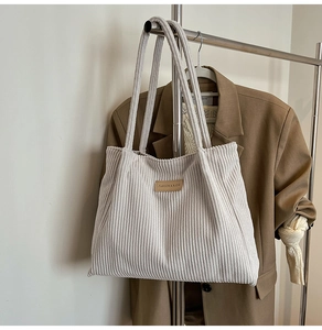 Detail of grey corduroy tote bag with brown leather patch on a hanging display