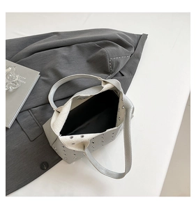 Close-up of light gray leather handbag with metal eyelets and pebble grain texture