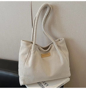 Detail of cream corduroy tote bag featuring a brown leather logo patch and soft texture