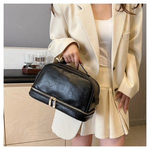 Detail of black vintage PU leather makeup bag with dual gold zippers and top handle