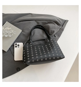 Detail view of black lychee leather bag with silver metal eyelets and a smartphone for size