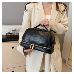 Detail view of large black leather makeup bag with dual zip storage and top handle