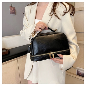 Detail of a black double-layer leather cosmetic bag with a handle and zipper compartments