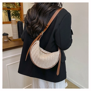 Dettaglio della borsa a mezzaluna in paglia beige con tracolla in pelle e fibbie