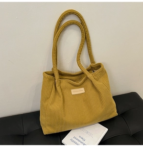 Close-up of yellow corduroy tote bag featuring leather logo patch and striped texture