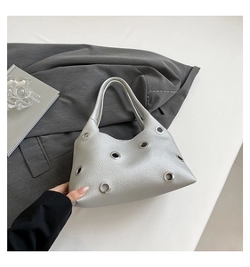 Detail view of silver crescent bag with metal eyelets on chic grey fabric background