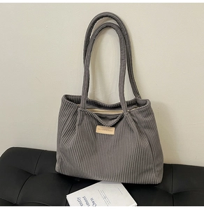 Detail of grey corduroy tote bag with leather label on a leather stool for daily commute