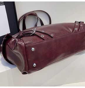 Detail view of burgundy leather tote with metallic eyelets and studded buckles