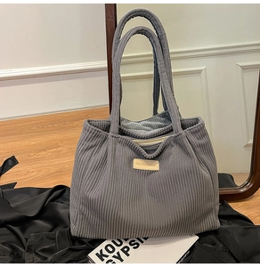 Close-up of dark grey corduroy tote bag showing ribbed texture and leather logo patch