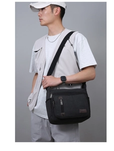 Detail of black canvas messenger bag with multi-zipper pockets and leather logo