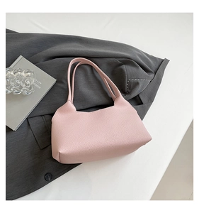 Pink pebbled leather shoulder bag placed on a grey blazer with stylish books and glass