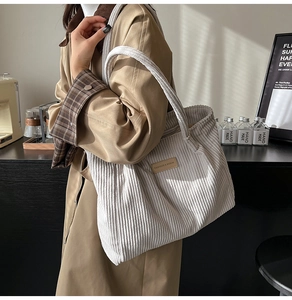 Close-up of white corduroy tote bag showing ribbed texture and brown leather brand patch