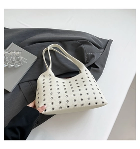 Detail of rivet cut-outs and lychee texture on a beige underarm bag over a grey blazer