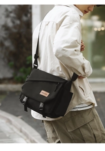 Close-up of black tactical messenger bag with dual buckles and adjustable wide strap
