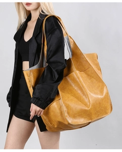 Detailed view of the large mustard yellow leather tote bag worn by a model on a grey background