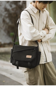 Detailed view of black messenger bag featuring flap buckle closure and leather brand logo