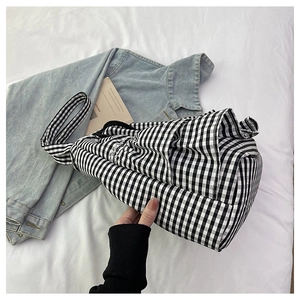 Detail view of a black and white gingham canvas tote bag placed on white bedding