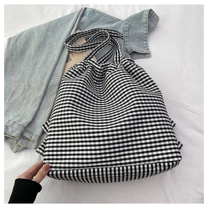 Detail of checkered canvas tote bag with wide straps on white bed linen background