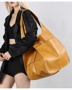 Side view of yellow large leather tote bag with wide strap on model in all black outfit