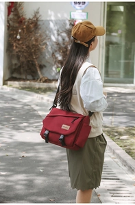 Macro detail of red nylon messenger bag featuring durable buckles and leather brand logo