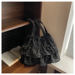 Vista detallada de un bolso tote negro con flores y volantes colgado en una estantería