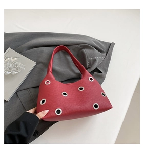 Detailed view of red leather shoulder bag featuring decorative silver metal eyelets and rivets