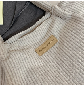 Detail of beige corduroy tote bag showing the leather logo tag and soft ribbed fabric