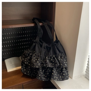 Detalle del bolso tote de gasa negra con volantes florales amarillos y cierre de cordón