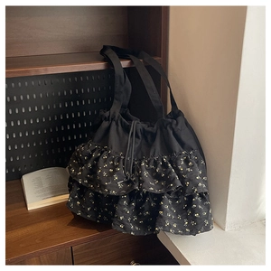 Detalle del dobladillo floral en el bolso negro con cordón sobre un estante de madera