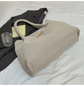 Detail of beige corduroy tote bag showing ribbed texture and leather patch on white cloth