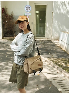 Detail of khaki nylon messenger bag with buckle closure and side pocket on outdoor model