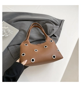 Detail of brown lychee leather handbag featuring silver metal eyelets and stitching