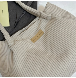 Detail view of beige corduroy tote bag featuring vertical texture and a leather patch