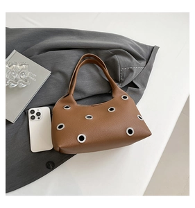 Close-up of brown litchi grain leather shoulder bag with silver metal grommet eyelets