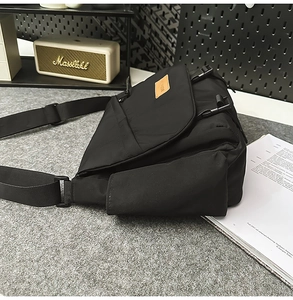 Black nylon messenger bag featuring a brown leather patch and adjustable shoulder strap