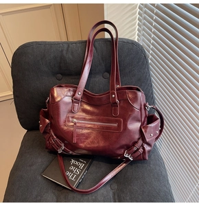 Close-up of vintage burgundy tote with silver zippers and rivet pockets on a dark chair