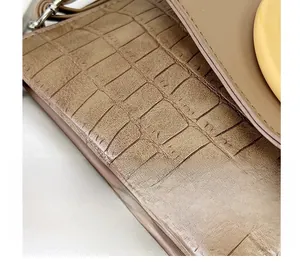 Detailed close-up of brown crocodile embossed leather texture with fine stitching on a bag